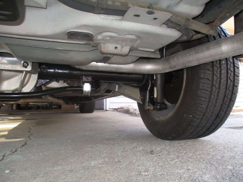 Underside view of a car's rear axle, exhaust pipe, and tire