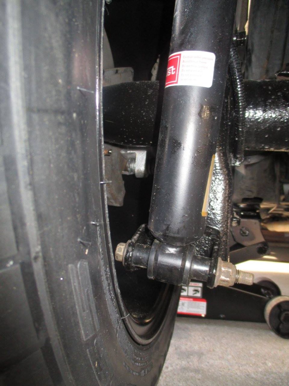 Close-up of a rear shock absorber and tire on a vehicle, with a red and white label on the shock