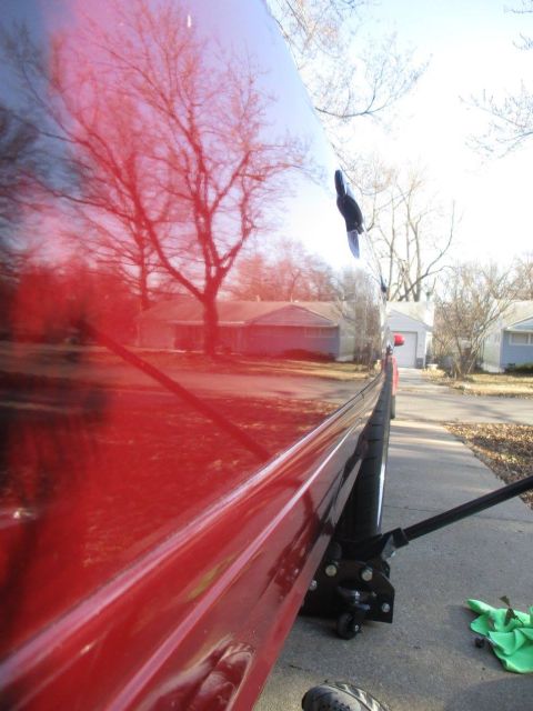 2004 Ford Crown Victoria - A red car's side is visible, reflecting trees and houses, with a jack positioned underneath.
