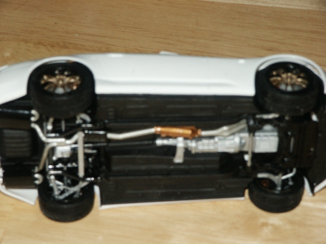 Underside view of a white car model, showing the exhaust and suspension components