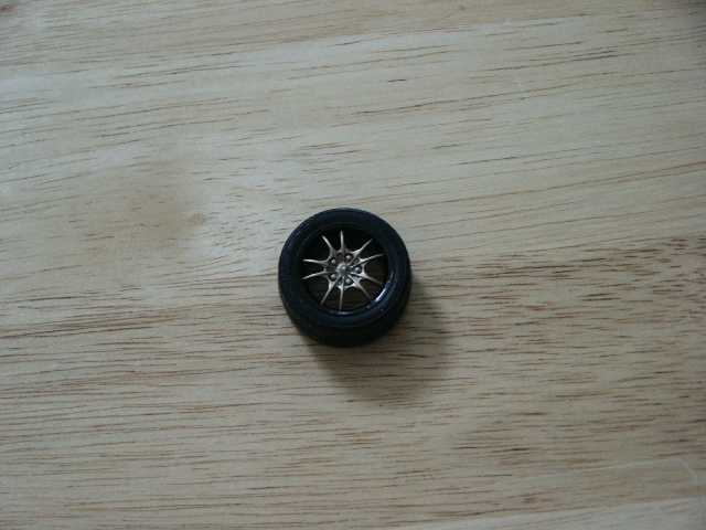 Wheel with silver multi-spoke rim and black tire on a wooden surface