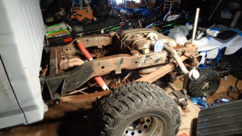 1985 Ford Bronco - The rear suspension and frame of a vehicle are visible, along with other vehicles and parts in the background.