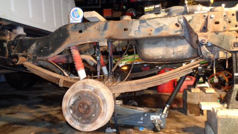 1985 Ford Bronco - The rear suspension system, including leaf springs and shocks, is visible on a vehicle being worked on in a garage.