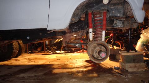1985 Ford Bronco - The vehicle's front suspension is disassembled, showing red shocks and coil springs.