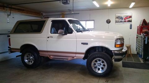 1994 Ford Bronco - Side view of a white Ford Bronco with tan trim and running boards, parked inside a garage.