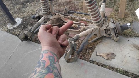 1991 Ford Bronco - Disassembled front axle and suspension components are shown, with a hand obscuring part of the view and giving the middle finger.