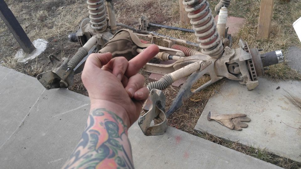 Disassembled front axle and suspension components with a hand giving the middle finger