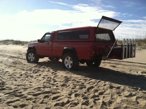 1991 Jeep Comanche - Red 1991 Jeep Comanche pickup truck with a camper shell and fishing rod holders parked on a sandy beach.