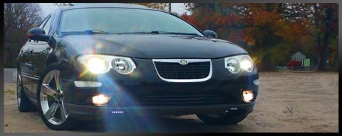 2002 Chrysler 300M - Front view of a black 2002 Chrysler 300M with headlights illuminated, parked outdoors with autumn foliage.
