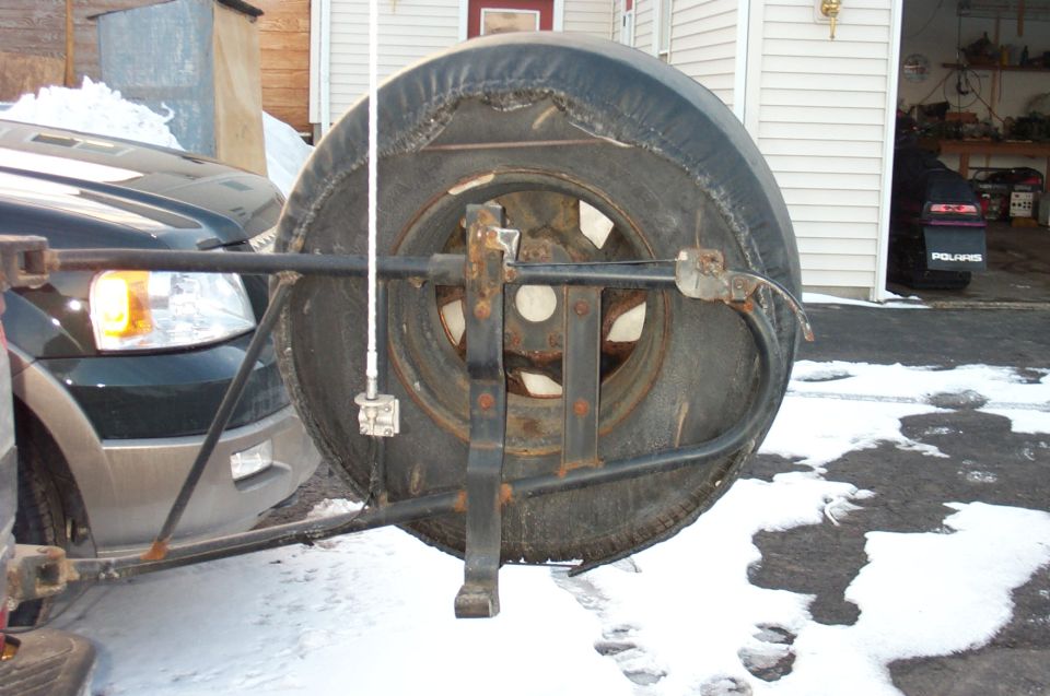 Swing-out spare tire carrier with torn black cover and CB antenna on a snowy driveway