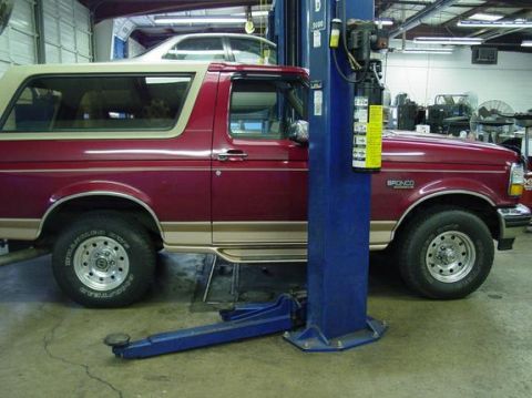1995 Ford Bronco - A red Ford Bronco is parked on a vehicle lift inside a garage, with another car visible in the background.