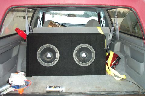 1995 Ford Bronco - The cargo area of a red SUV contains a large subwoofer box and various items, obscuring any specific year identification.