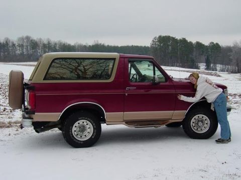1995 Ford Bronco - A woman hugs a maroon and tan Ford Bronco in a snowy field.