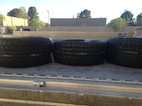 2010 Dodge Challenger - Several tires are loaded onto a truck bed, with a building and trees in the background.