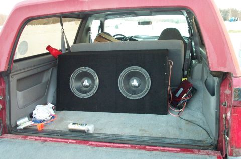 1995 Ford Bronco - The rear cargo area of a red SUV contains a large subwoofer box with two speakers and an amplifier.