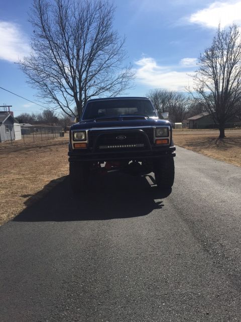 1982 Ford Bronco - This lifted Ford Bronco is shown from the front on a sunny day, with a residential area visible behind it.