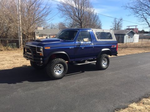 1982 Ford Bronco - A blue Ford Bronco is parked on a residential street under a clear sky.