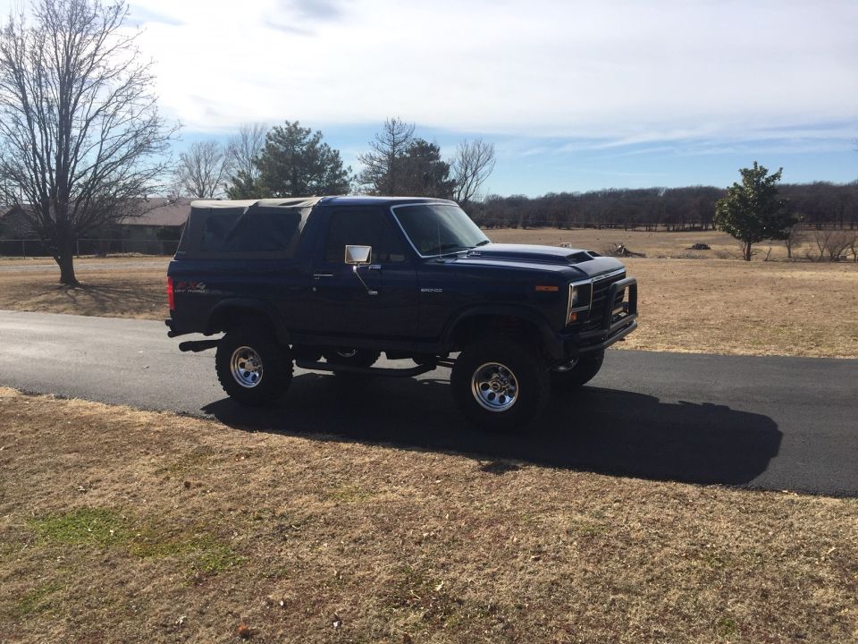 Dark blue 1982 Ford Bronco with soft top, lifted, on a paved road