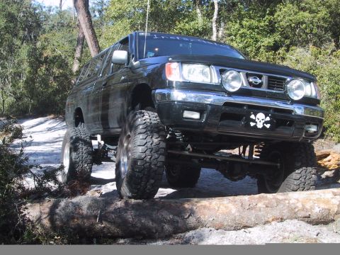 1991 Ford Bronco - Modified black Nissan SUV navigates an obstacle on a wooded trail.