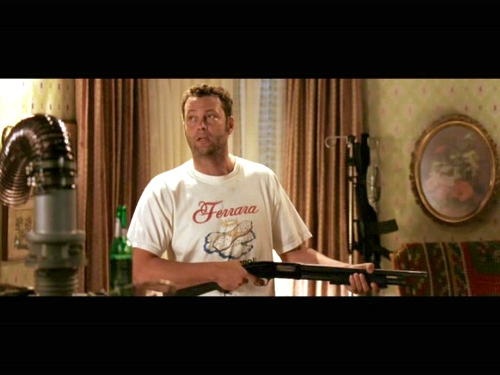 Man holding a pump shotgun indoors in a film still, Ferrara T-shirt