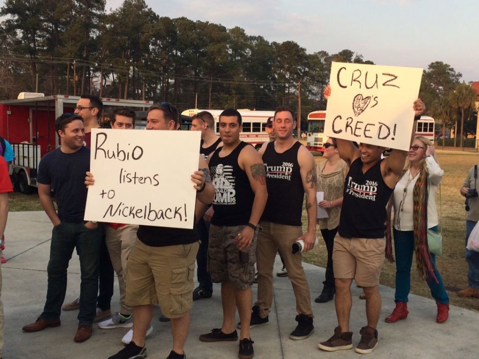 Group of men holding political protest signs at an outdoor rally