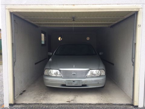 1999 Ford Fairlane - A silver sedan is parked inside a garage. The front of the vehicle is visible, showing its headlights, grille, and bumper.
