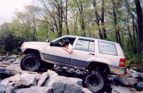 1978 Ford Bronco - A silver SUV is shown off-roading over a pile of large rocks.