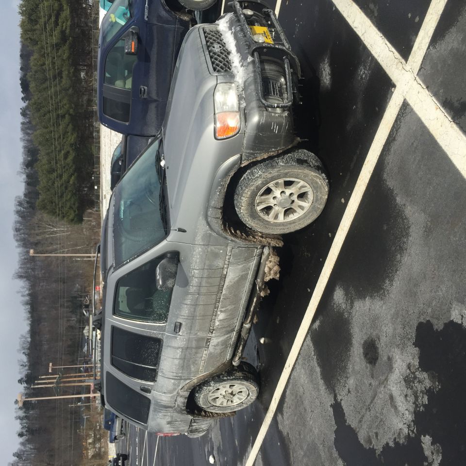 Muddy and snow-covered gray SUV parked in a wet parking lot.