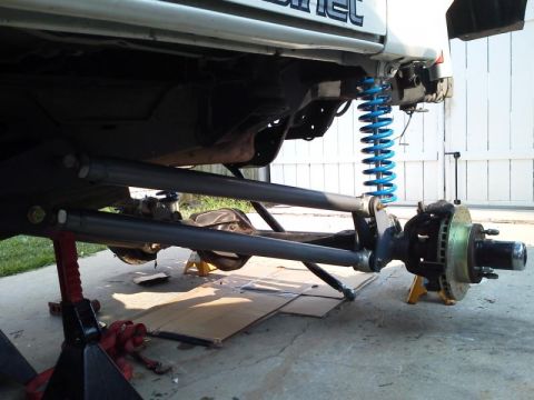 1981 Ford Bronco - The underside of a modified vehicle, likely a 1981 Ford Bronco, is shown with custom suspension components including bright blue coil sprin…