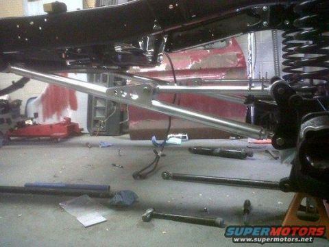 1981 Ford Bronco - The underside of a vehicle is shown, focusing on the suspension system and frame. Several metal bars and a large coil spring are visible, a…