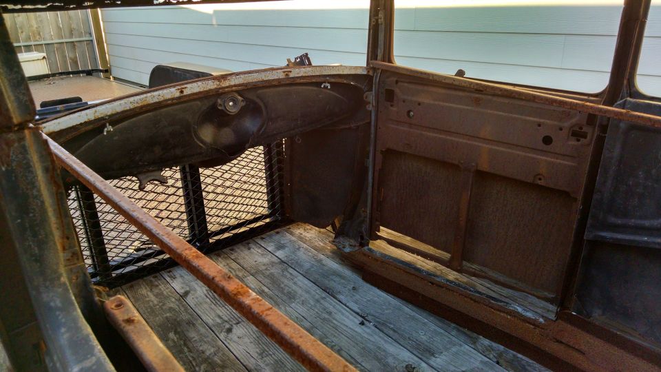 Interior of a rusty vintage car showing wooden floor, metal door, and dashboard.