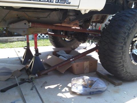 1981 Ford Bronco - The undercarriage of a lifted vehicle, likely a 1981 Ford Bronco, is supported by red jack stands. Red metal bars extend from the frame to…