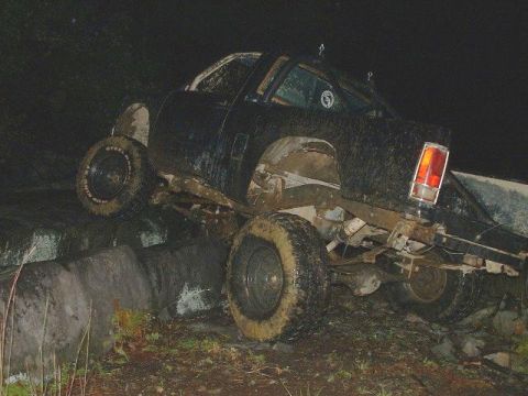 1978 Ford Bronco - Off-road vehicle tires are caked in mud as it climbs over large rocks in the dark.