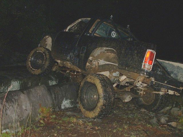 Mud-covered off-road vehicle with large tires navigating over rocks at night