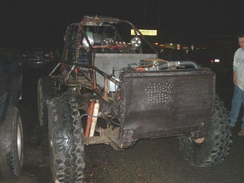 1978 Ford Bronco - A heavily modified off-road buggy with oversized tires and a custom body sits parked at night, next to another vehicle.
