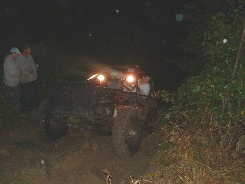 1978 Ford Bronco - A group of people stand near a heavily modified off-road vehicle on a muddy path at night.