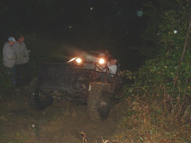 Muddy buggy with roll cage and bright headlights on a dark trail at night