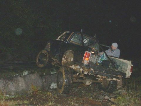1978 Ford Bronco - A mud-covered 1978 Ford Bronco with a roll cage is tilted on a dirt embankment at night.