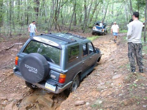 1978 Ford Bronco - A Toyota 4Runner navigates a challenging off-road obstacle, with another vehicle and onlookers present in the wooded terrain.