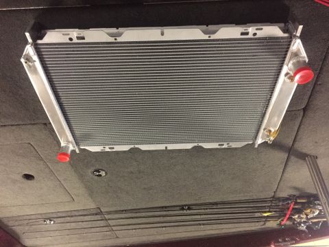1982 Ford Bronco - A large aluminum radiator with red caps on the inlet and outlet ports is installed in a vehicle. The radiator is positioned horizontally an…