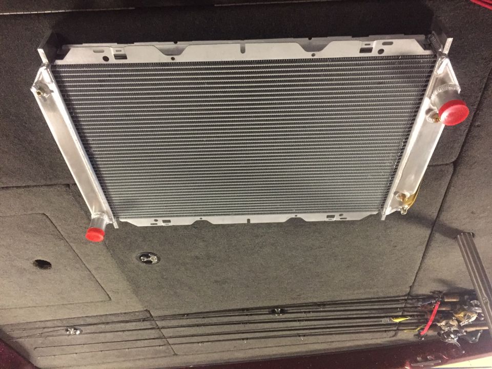 Close-up of a custom aluminum radiator with red caps, installed in a vehicle.