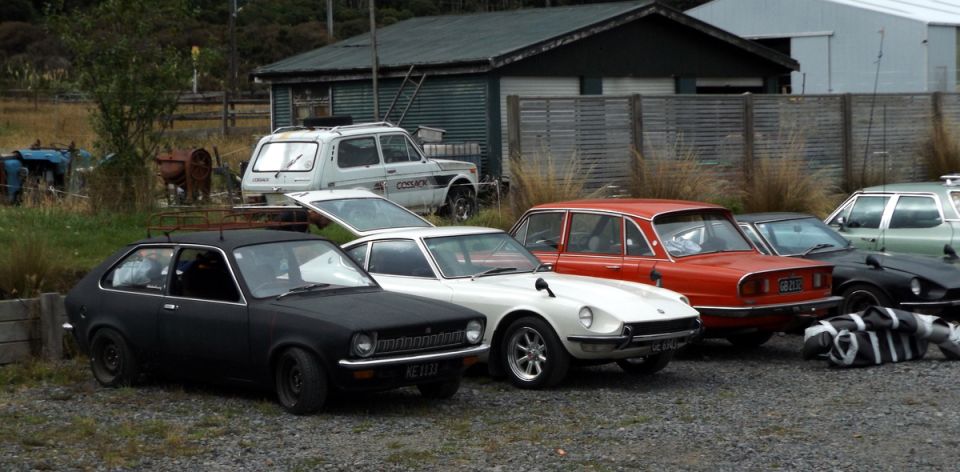 Various vintage cars parked on gravel in front of a building.