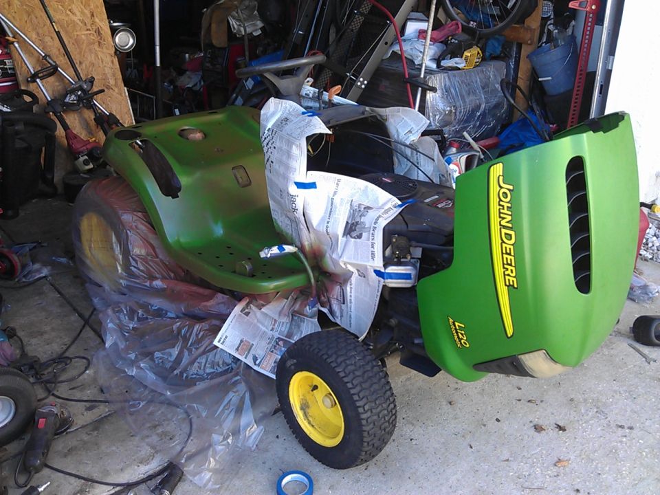 Green John Deere L120 lawn tractor with plastic sheeting and newspaper.