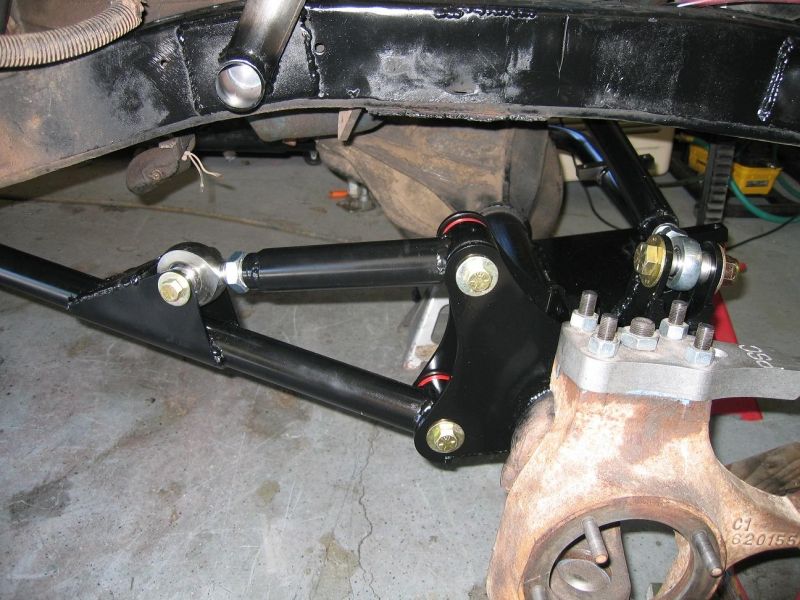 Close-up of vehicle suspension with black tubular control arms and spindle.