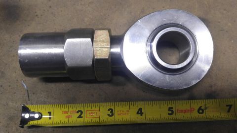 1991 Ford Bronco - A metal rod end with a bearing and a threaded shaft is shown next to a yellow measuring tape. The rod end is silver and has a gold-colored…