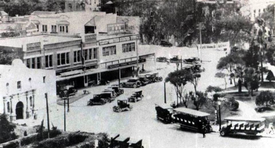 Street scene with numerous early 20th-century automobiles parked and driving near historic buildings