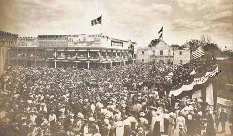 1909 Ford Model T - A large gathering of people in front of buildings, possibly a fair or event, with American flags visible.