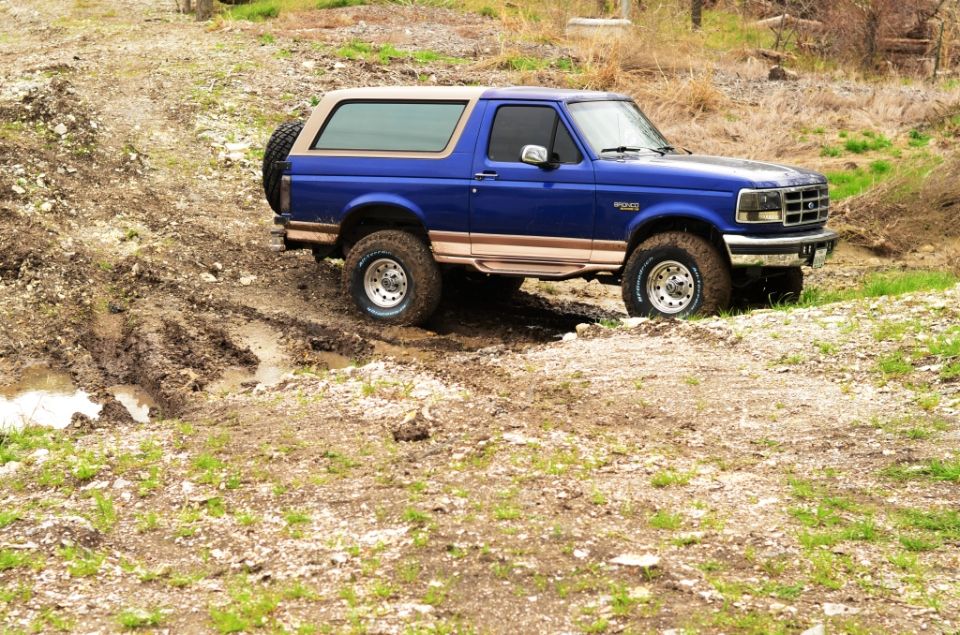 Blue 1996 Ford Bronco driving through a muddy trail