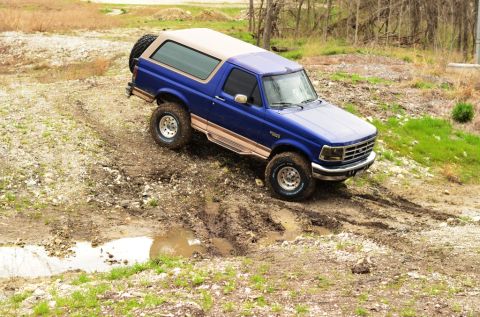 1996 Ford Bronco - A blue 1992 Ford Bronco navigates a muddy off-road trail.