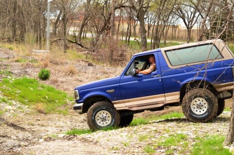 1996 Ford Bronco - A blue 1996 Ford Bronco navigates an off-road trail with a tan top.